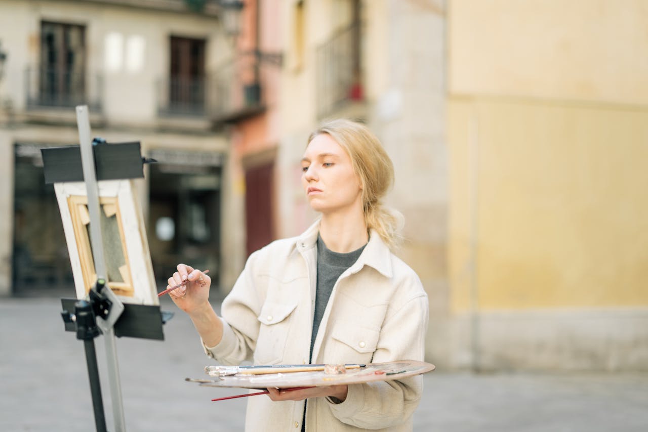 Caucasian woman painting on street with easel and palette in urban area.